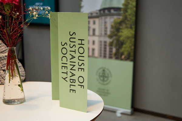 Close-up shot of one of the tables during the fika break at the HoSS Forum 2026, displaying a green leaflet about the House of Sustainable Society and banner in the background.