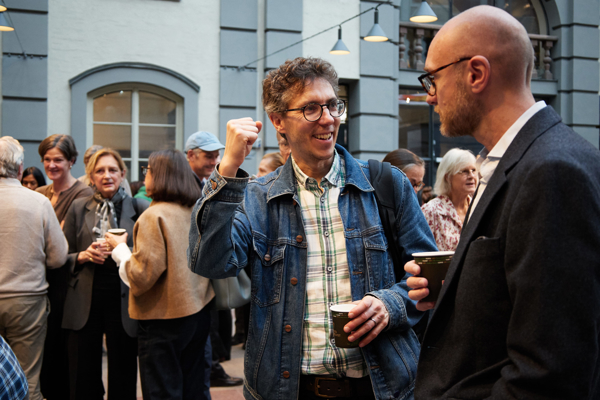 Close-up shot of two men talking and laughing in a packed Atrium at the Stockholm School of Economics during the fika break at the HoSS Forum 2026.