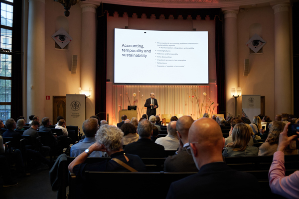 Wide shot of Professor Michael Power delivering his academic address during the HoSS Forum 2026 in a full Aula at the Stockholm School of Economics.