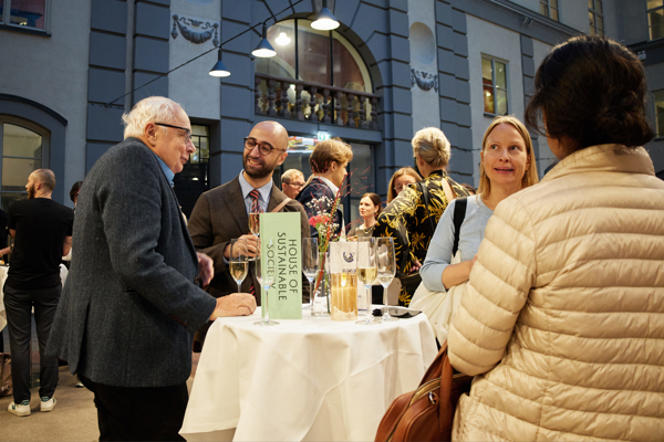 Close-up of a group of people deep in discussion during the mingle after the HoSS Forum 2026 in a full Atrium at the Stockholm School of Economics.