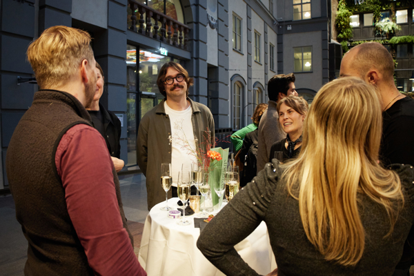 Close-up of a group of people chatting and laughing during the mingle after the HoSS Forum 2026 in a full Atrium at the Stockholm School of Economics.