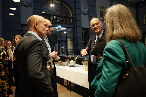 Close-up of a group of people, including Professor Michael Power and Center Director Torkel Strömsten, talking and laughing during the mingle after the HoSS Forum 2026 in a full Atrium at the Stockholm School of Economics.