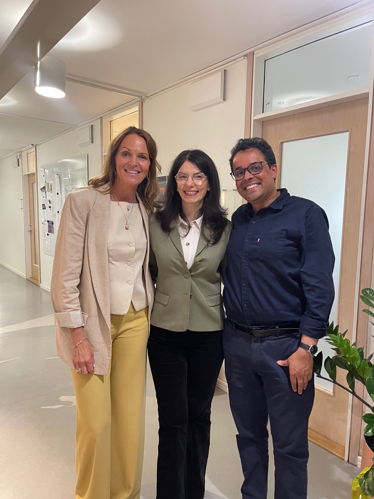Avenia Ghazarian standing in a corridor at the Stockholm School of Economics with her primary supervisor, Martina Björkman Nyqvist, to her right and her secondary supervisor, Abhijeet Singh, to her left.