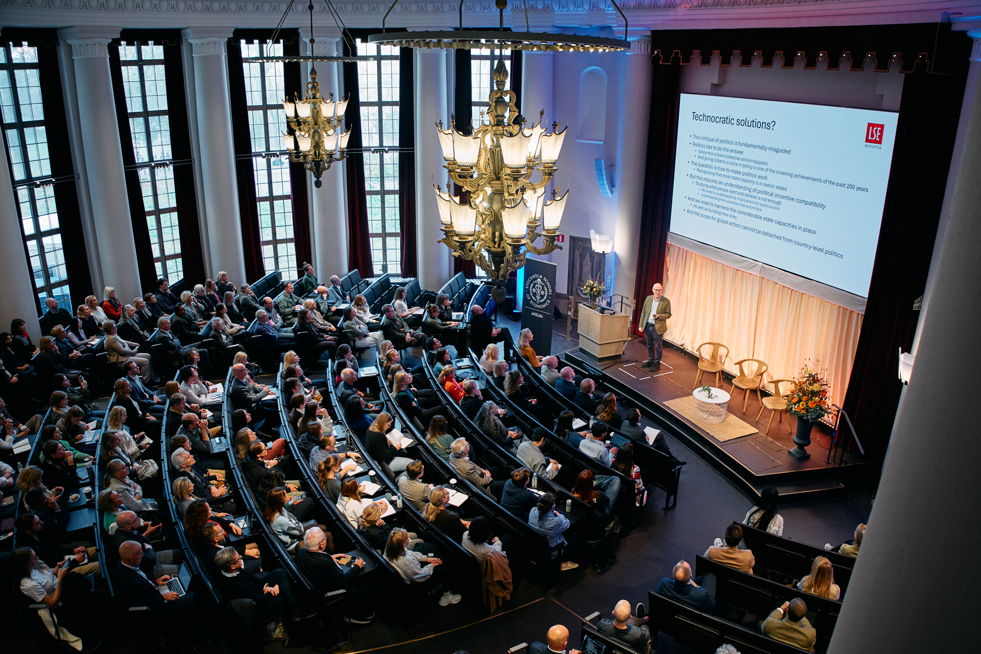 A filled aula at Stockholm School of Economics, with a speaker at the front presenting sustainability research.