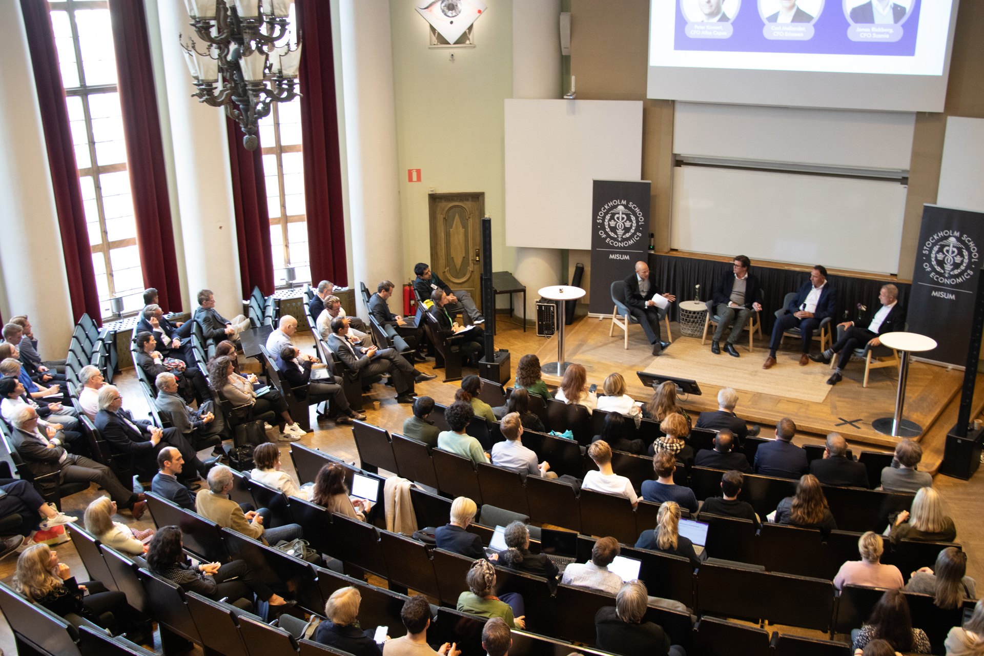 An auditorium full of people listening to a panel discussion on stage.