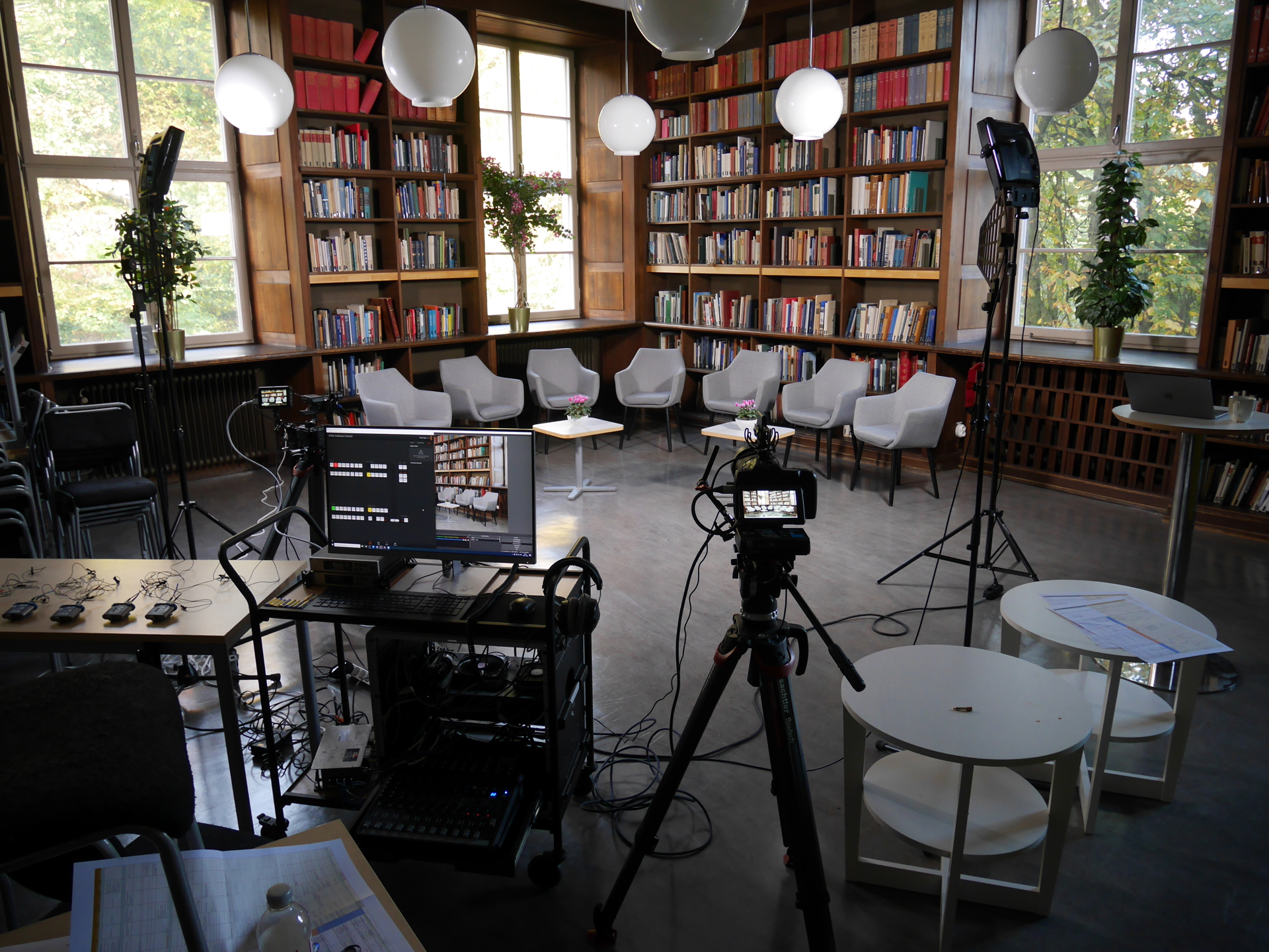 Several chairs standing in a half-circle in front of walls covered with bookshelves, with a camera in the foreground ready to start recording the session.