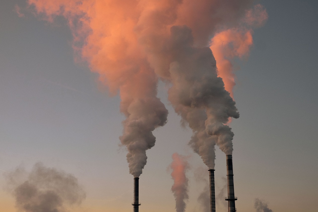 Industrial emission fumes rising against the sky during a sunset.