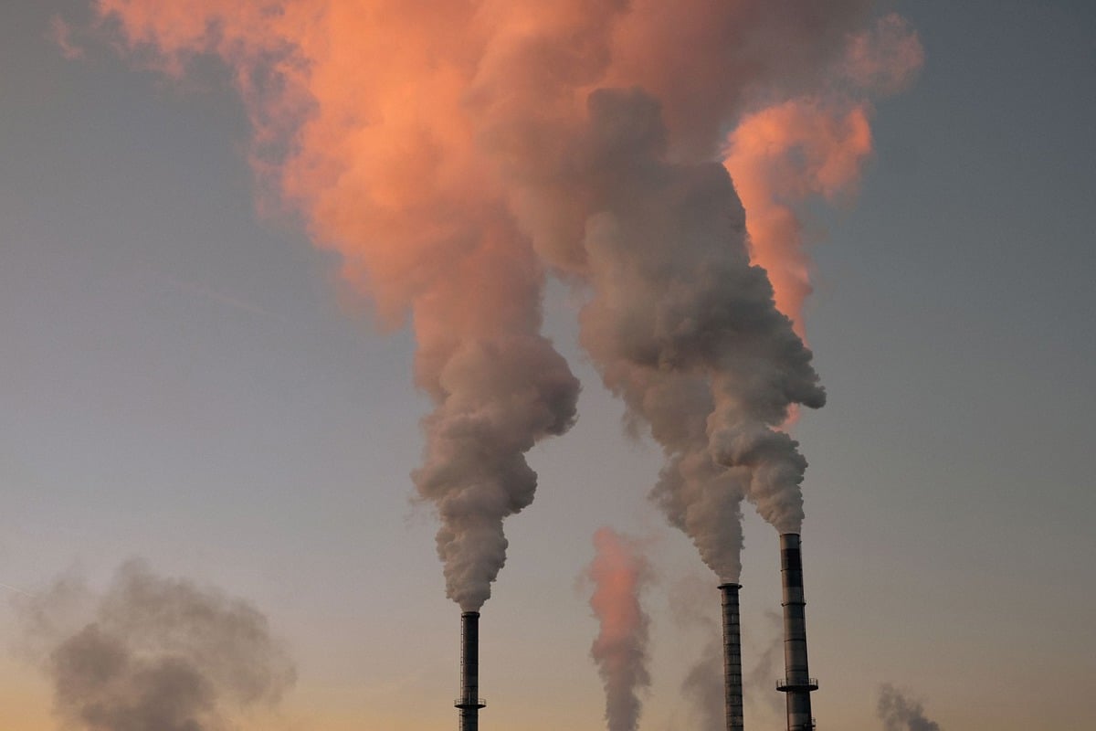 Industrial emission fumes rising against the sky during a sunset.