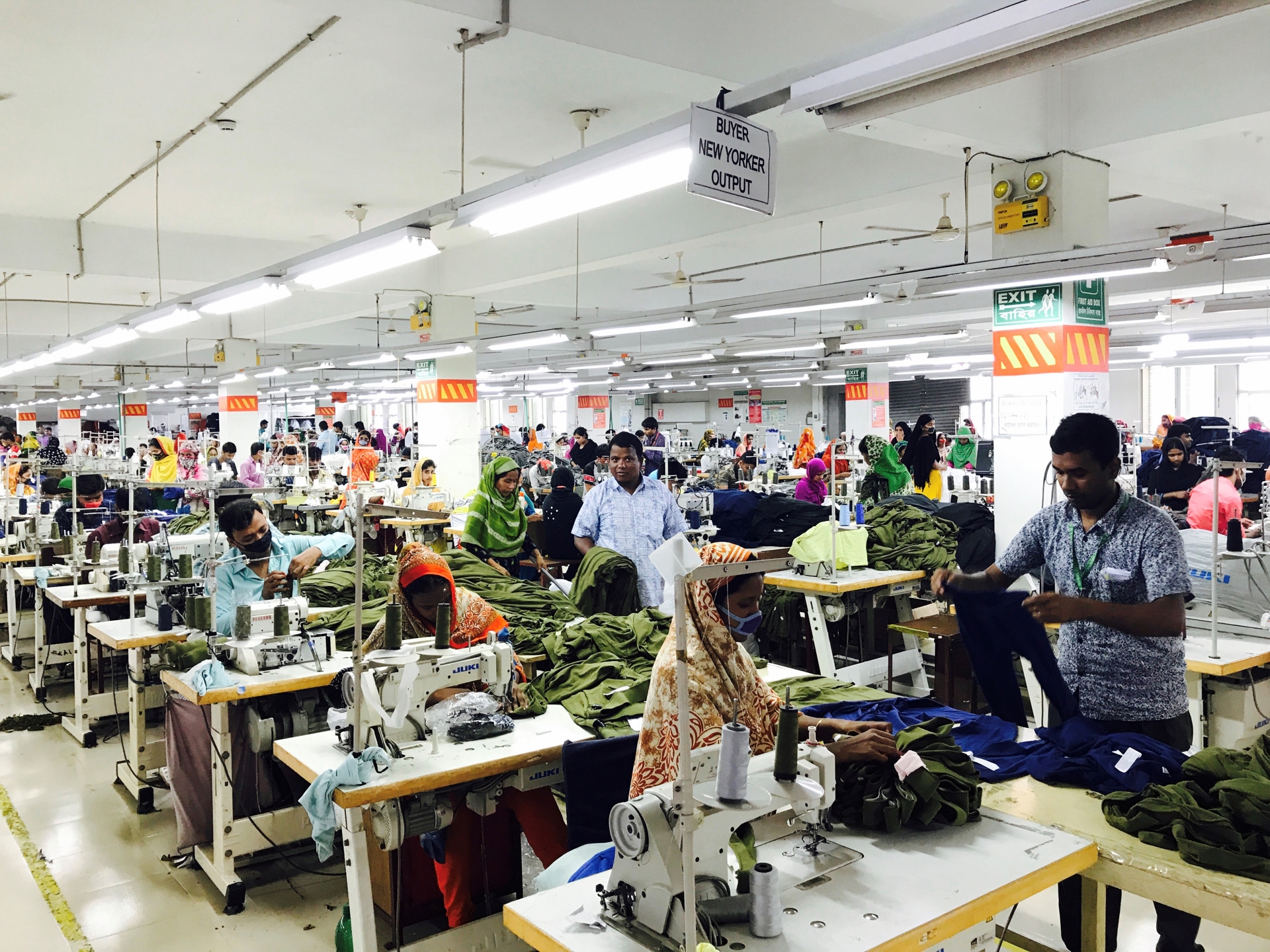 Apparel supply chain in Bangladesh. Men and women sit by sewing machines, managers walk the corridors inspecting the work.