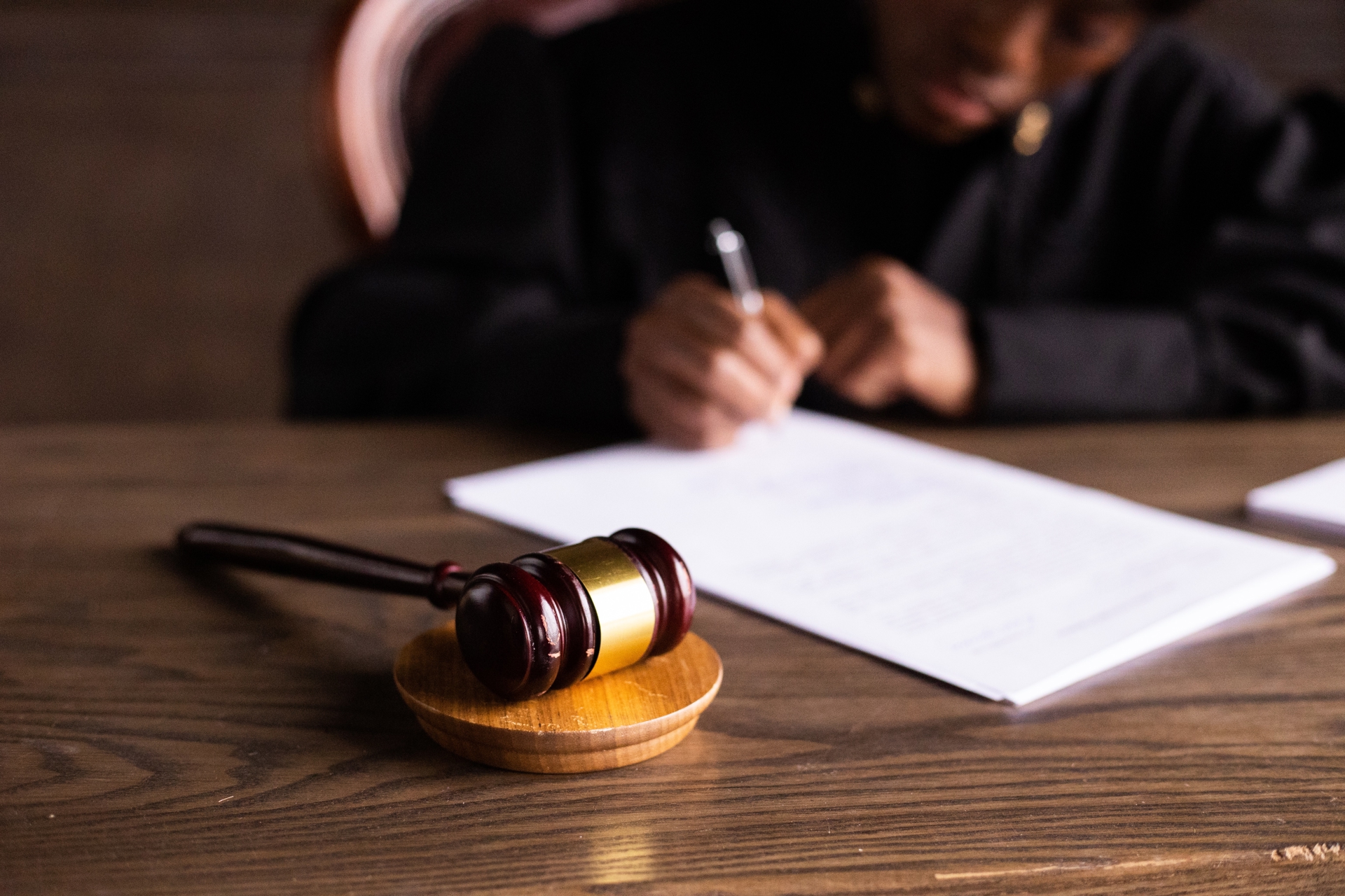 Judge's gavel sitting on a desk with a person sitting writing a long document in the background