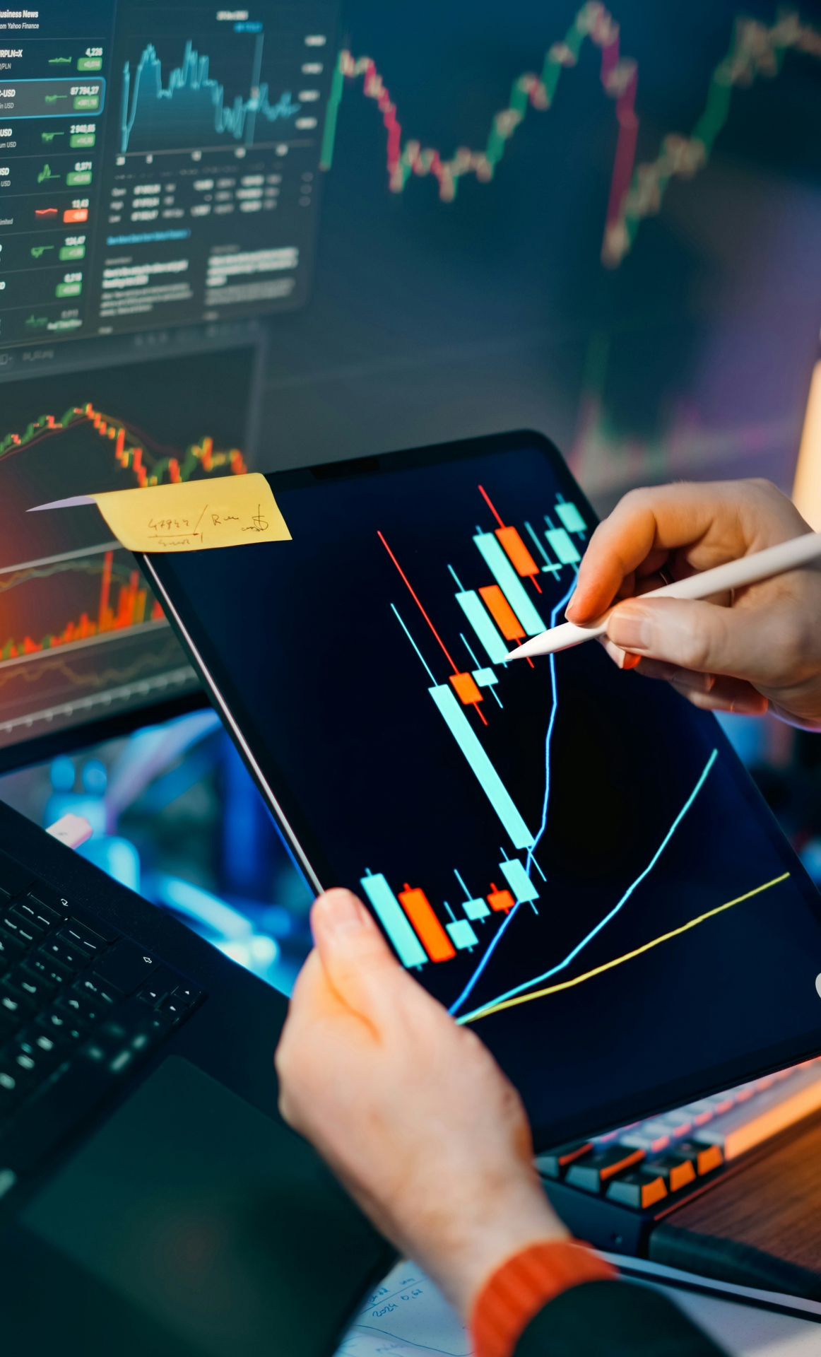 Person holding a tablet in front of a computer screen, depicting various graphs of the financial market.