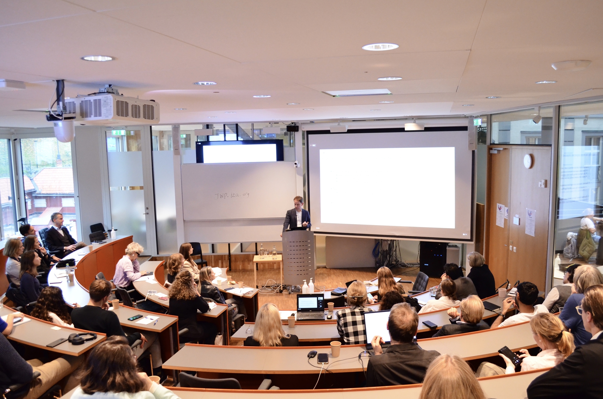 A researcher holding a lecture at the Stockholm School of Economics in front of a full room consisting of students, professionals in academia, industry leaders, and policymakers.