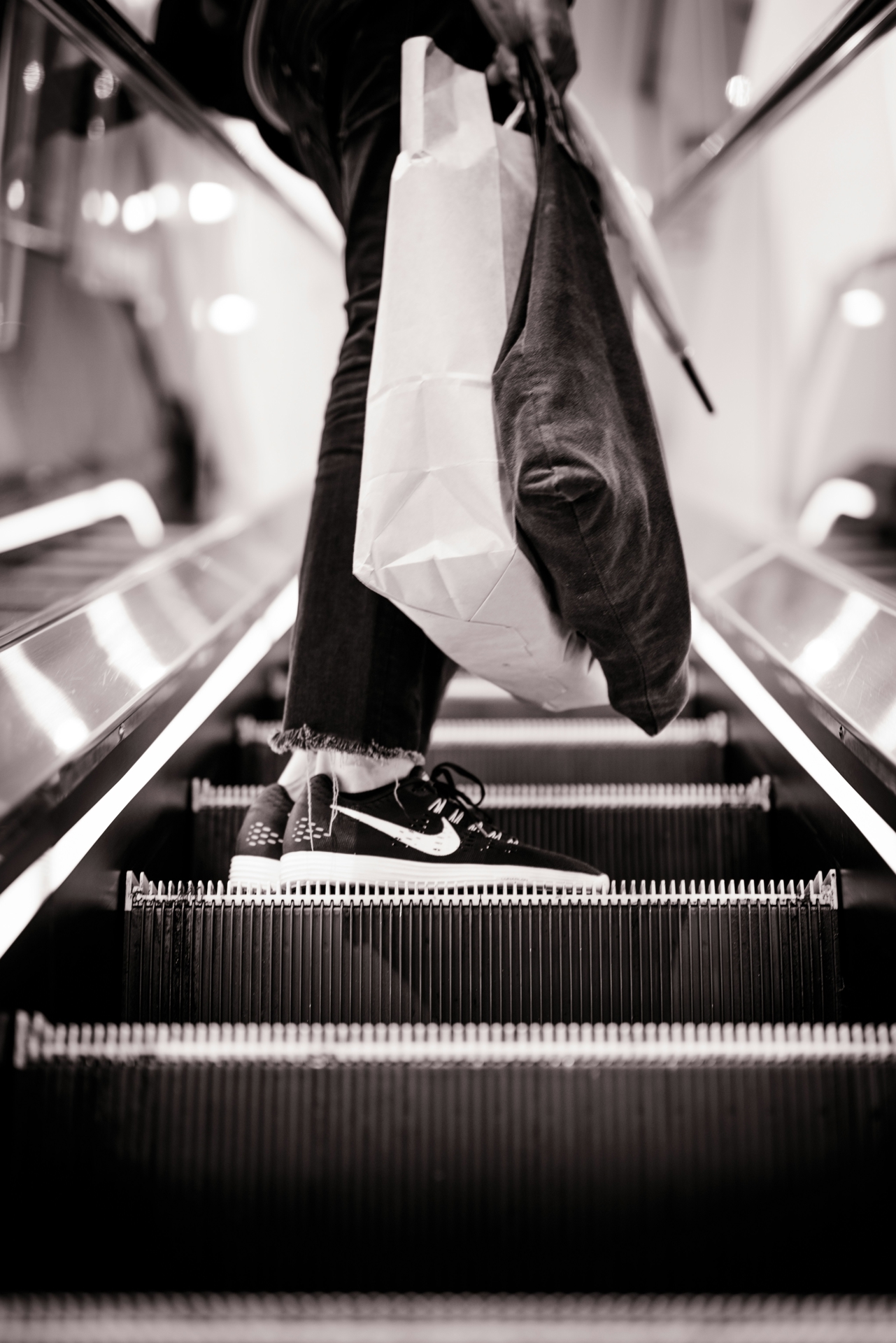 Person standing on an escalator holding two shopping bags.