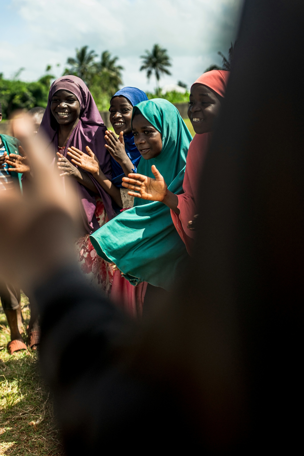 A group of hooded women standing in a half-circle looking happy and clapping.