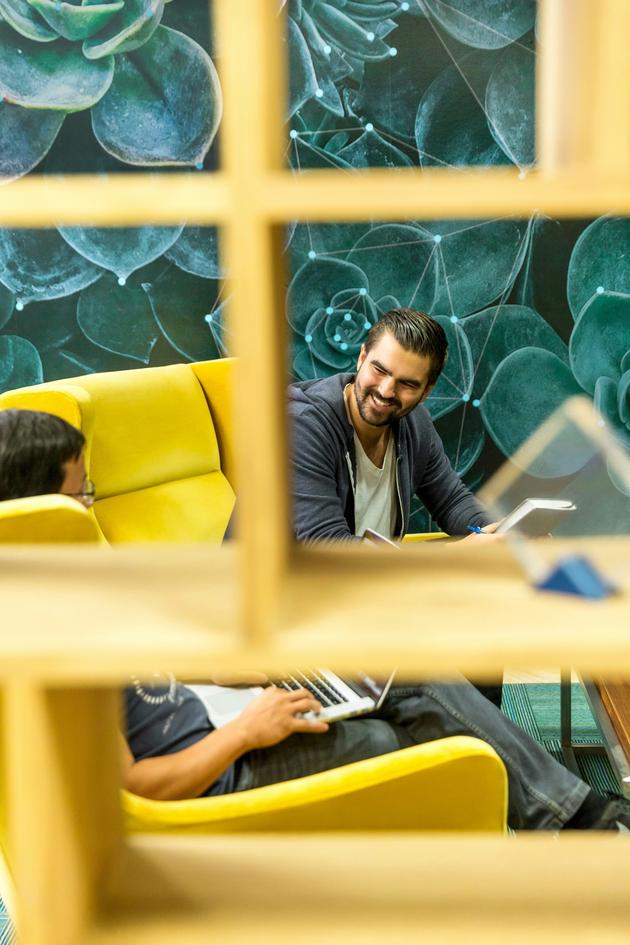 A manager sits smiling in conversation with an employee on a yellow couch.