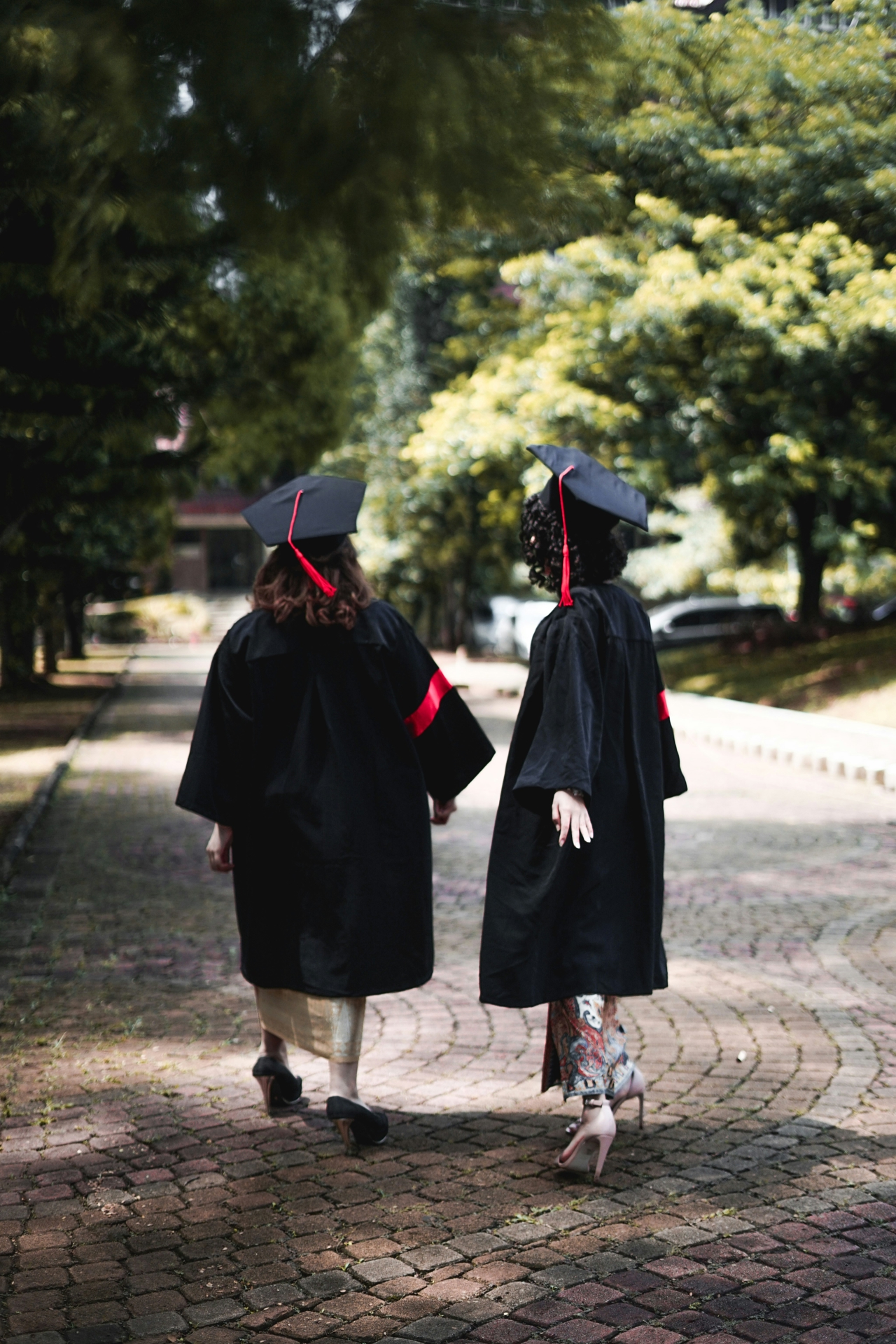 Two female students walking down a tree-lined street in their graduation robes.