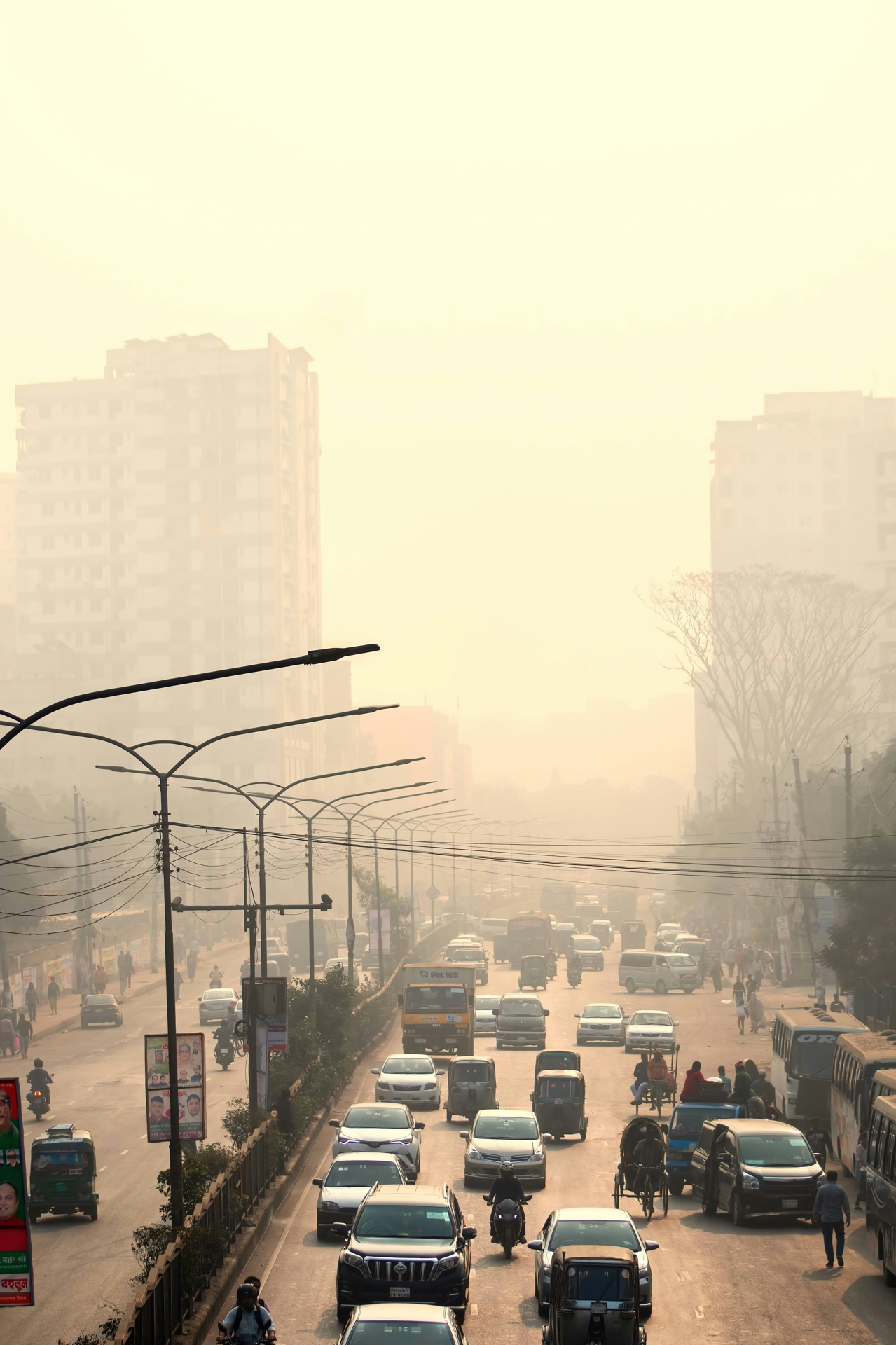 Street with a lot of traffic, in the background city buildings are barely discernable through a smog. 