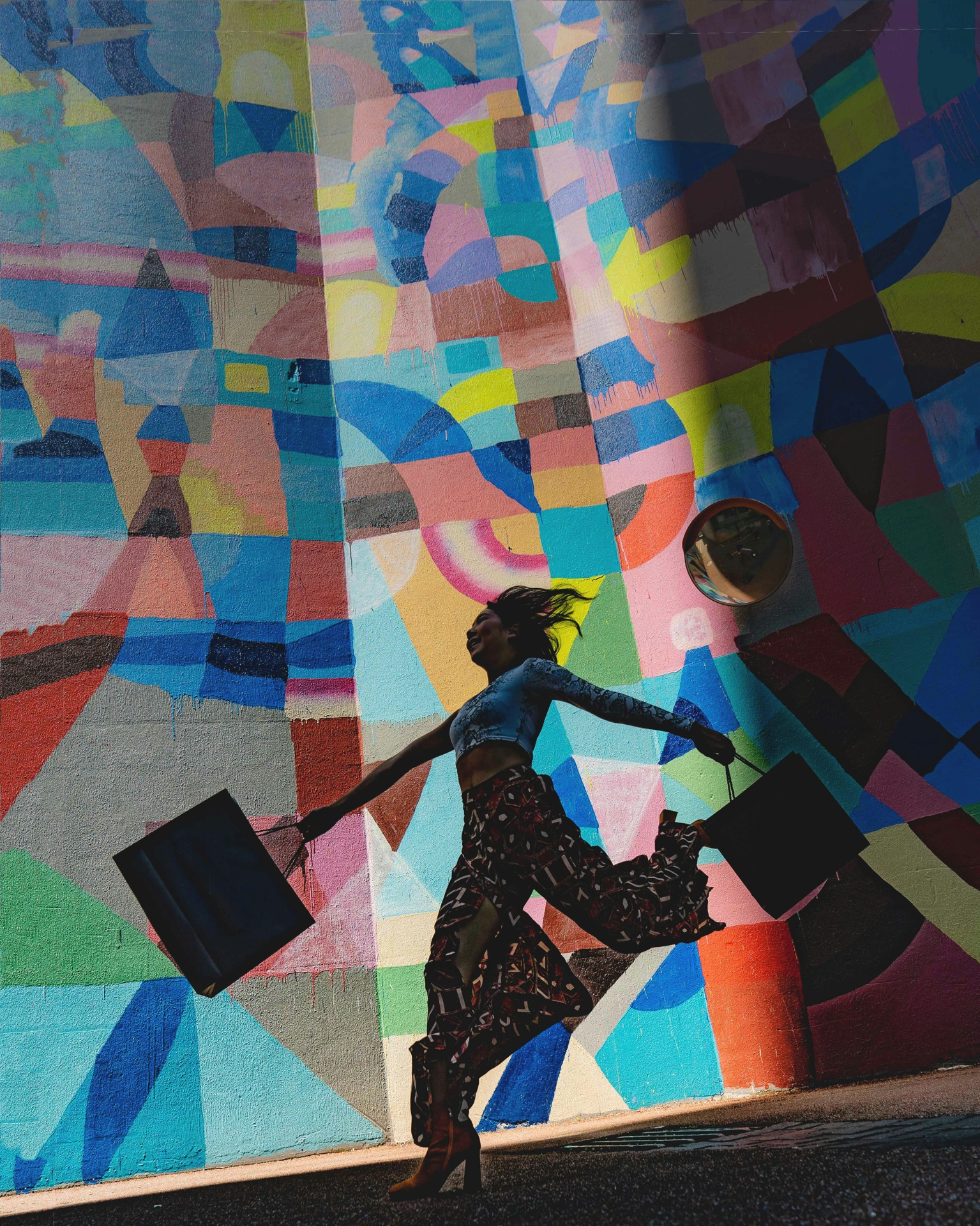 Woman skipping with a shopping bag in each hand against a colorful wall mural outside.