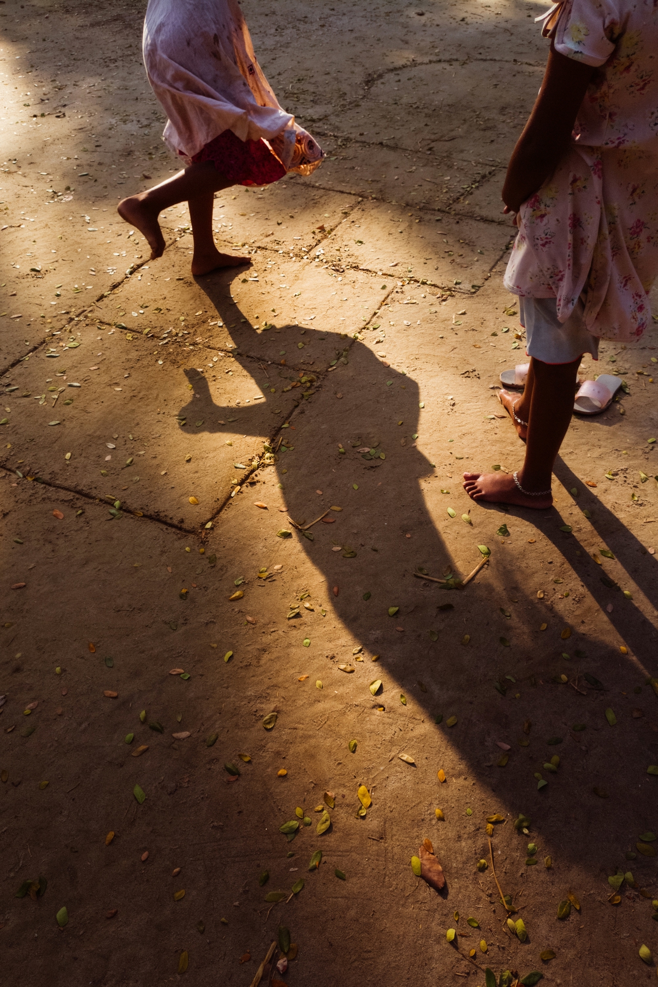 Two shadows of children playing in the sunset against a sandy ground