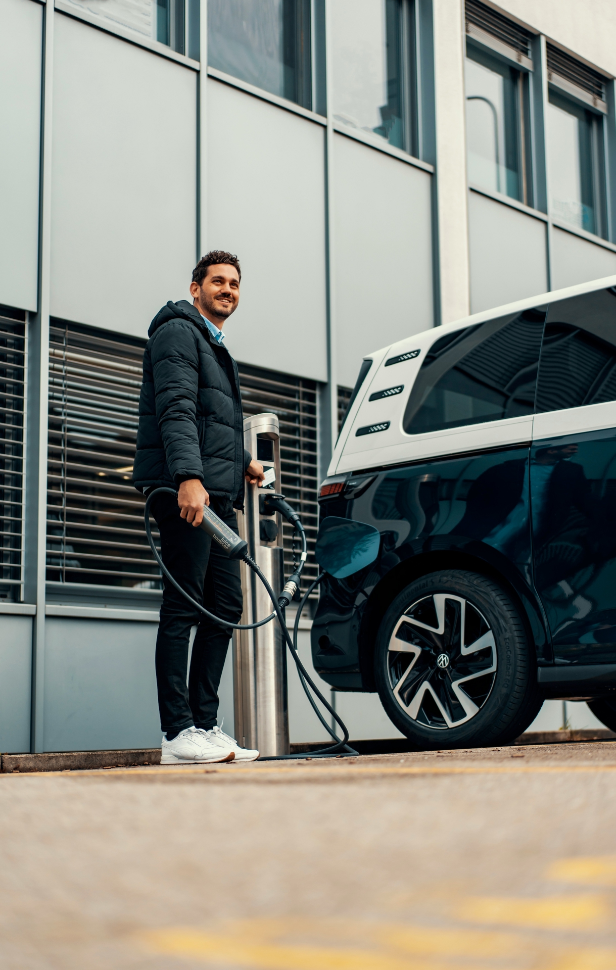 Man standing by his electric vehicle, plugging in the charger cable. 