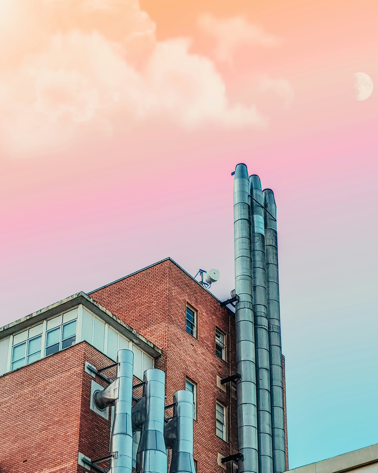 Industrial building in brick and metal against a sky painted in different shades of pink by the sunset.
