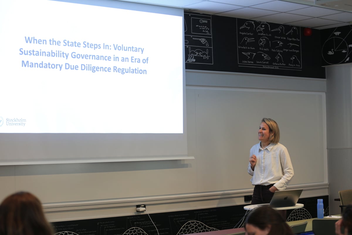 Julia Grimm standing next to a projector, smiling while presenting her latest research at a Green Bag seminar at the Stockholm School of Economics.