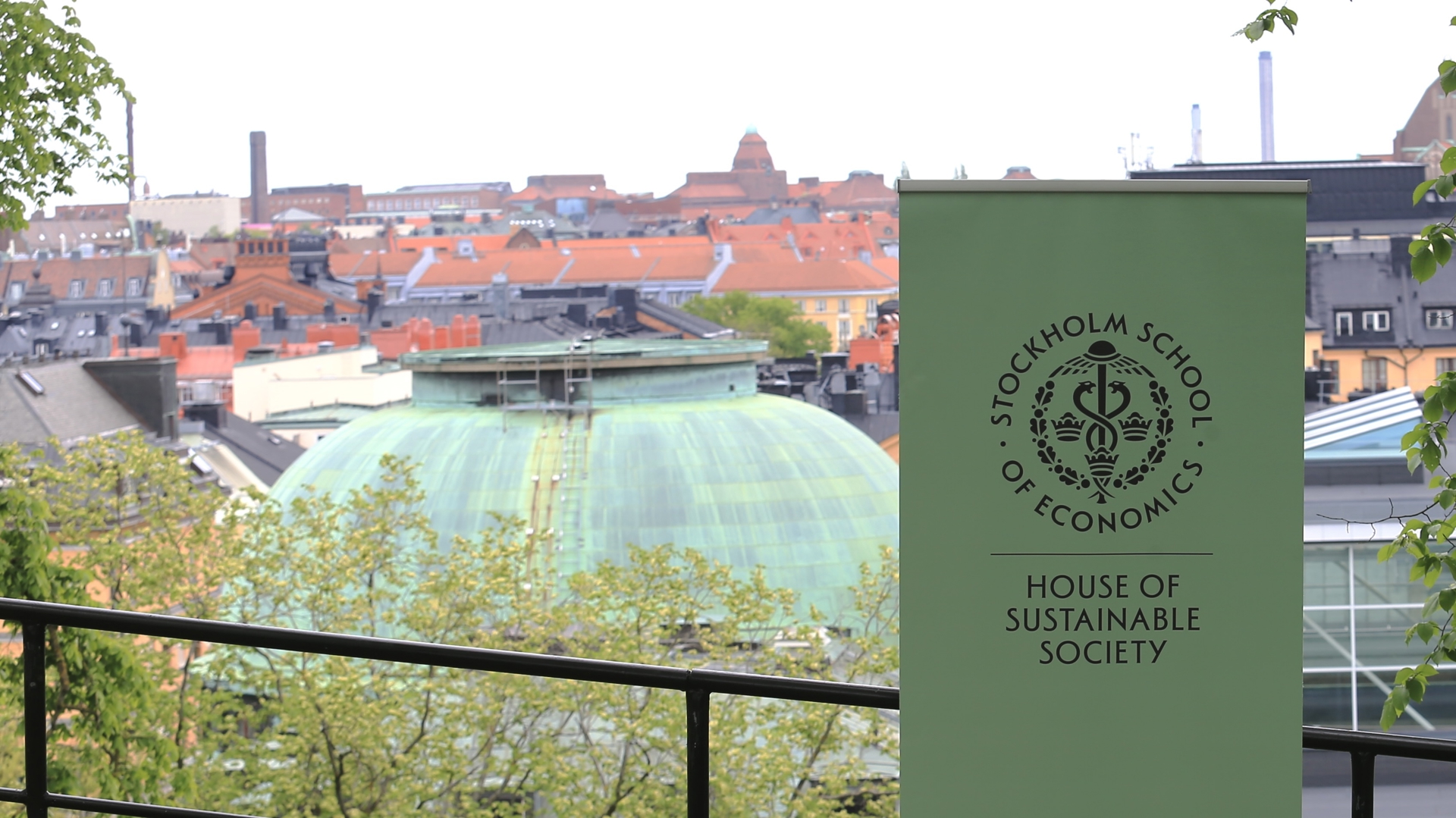 A green banner with the logo for the House of Sustainable Society of the Stockholm School of Economics, with the School in the background.